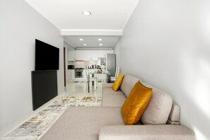 Een modern interieur met een bank, een flatscreen televisie en een keuken op de achtergrond.