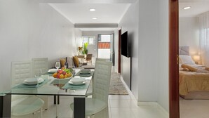 A modern dining area with a glass table, white chairs, and a fruit bowl.