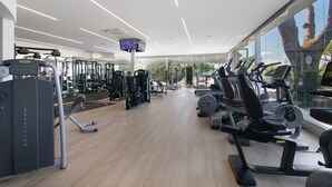 Een fitnessruimte met diverse trainingsapparaten, een televisiescherm en grote ramen.