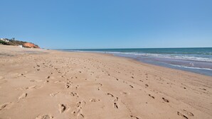 Een zandstrand met voetafdrukken, een heldere lucht en een verre kustlijn.
