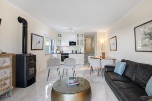 Een moderne woonkamer met een glazen salontafel, een zwarte leren bank en een keuken op de achtergrond.