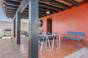 Une terrasse extérieure avec une table et des chaises, un banc bleu et un barbecue.