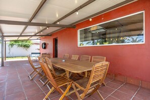 Eine überdachte Terrasse mit einem Holztisch und -stühlen, einem großen Fenster und einer roten Wand.