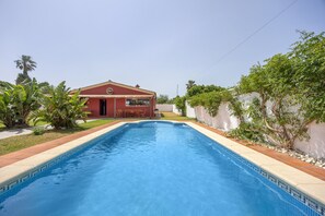 Ein rechteckiger Pool mit einer gefliesten Kante, umgeben von einem roten Gebäude mit einem Ziegeldach und einer weißen Mauer mit Pflanzenbewuchs.