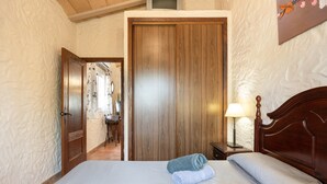Habitació d'hotel amb una porta de fusta, un llit amb roba blanca, una tauleta de nit amb una làmpada i vista a un passadís.