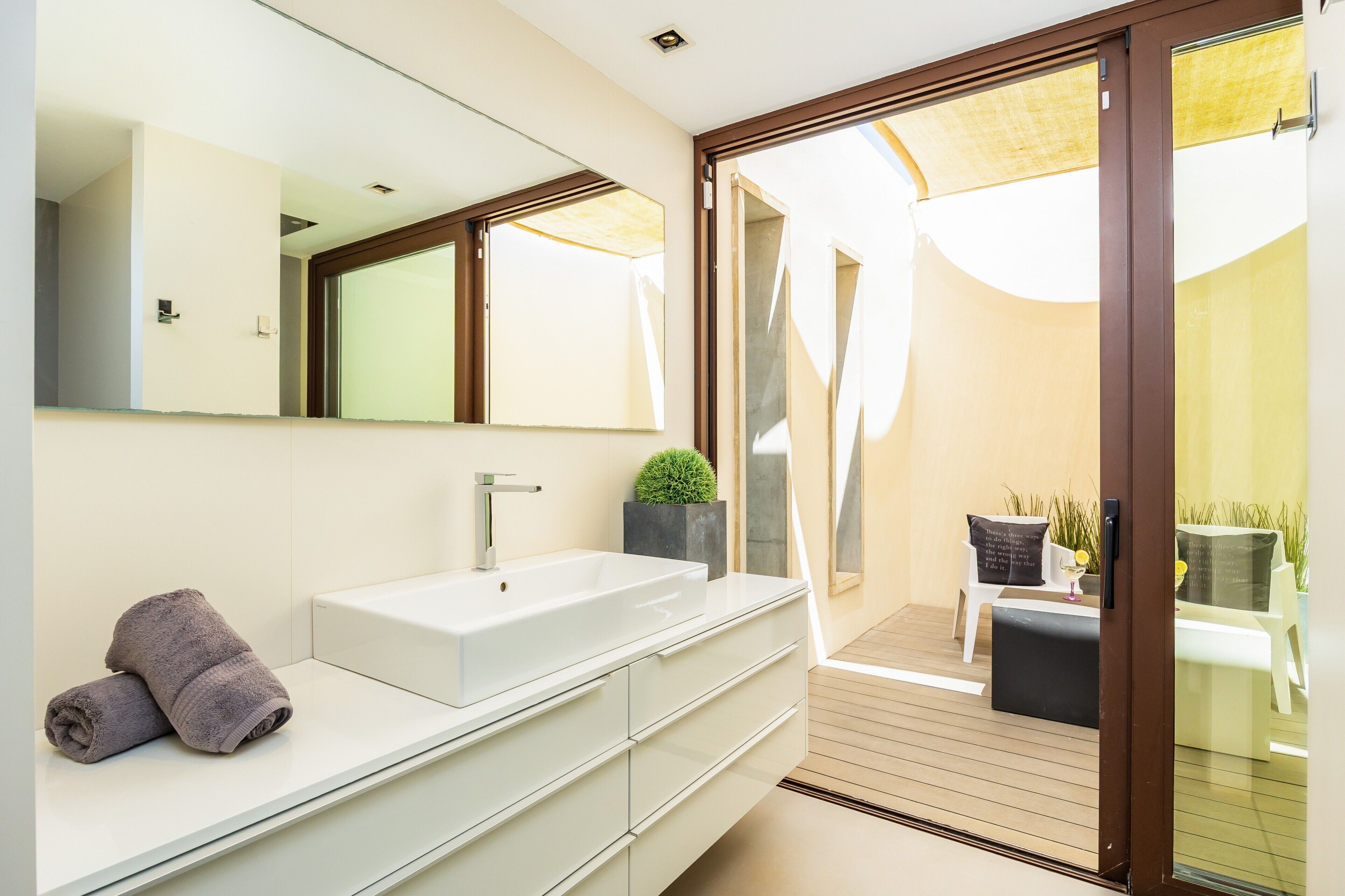A modern bathroom with a large mirror, white vanity, and a towel on the counter.