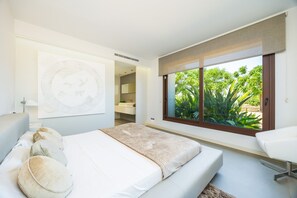 A modern bedroom with a large bed, a bedside table, a window with a view of greenery, and a bathroom visible through an open door. - Country House 'S'Hort' with Mountain View, Wi-Fi and Air Conditioning (Muro)