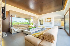 A modern living room with a beige sofa, a white coffee table, and a large window offering a view of greenery. - Country House 'S'Hort' with Mountain View, Wi-Fi and Air Conditioning (Muro)