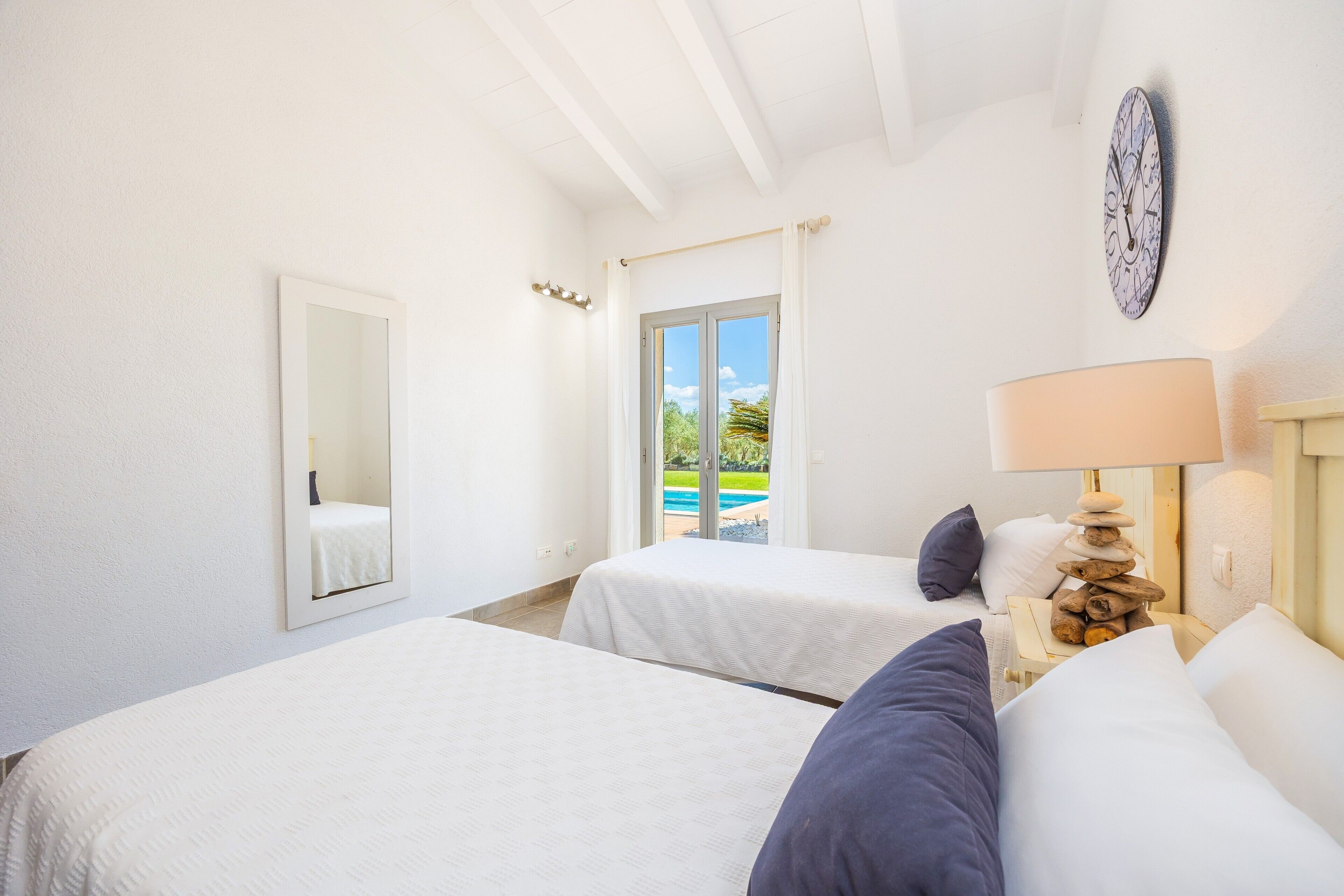 Habitación de hotel con dos camas, un espejo grande, una lámpara y vistas a una piscina.