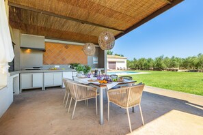 Une cuisine extérieure avec une table et des chaises, une piscine en arrière-plan et un ciel dégagé.
