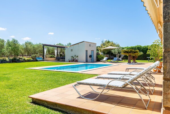 Une piscine avec des chaises longues, un petit bâtiment et un jardin.