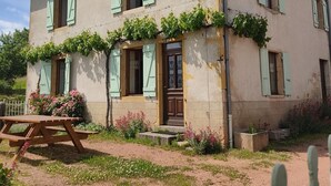 A two-story house with green shutters, a wooden bench, and a garden with flowers and vines. - Les Alognes - TANCON (TANCON)