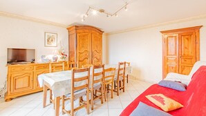 A dining area with a wooden table and chairs, a television on a wooden cabinet, and a red sofa with cushions. - Les Alognes - TANCON (TANCON)