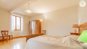 A bedroom with a bed, a wooden wardrobe, a chair, a table, a lamp, and a window with curtains. - Les Alognes - TANCON (TANCON)