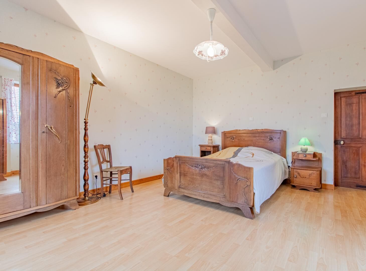 A bedroom with a wooden bed, a nightstand, a chair, a wardrobe, and a chandelier.