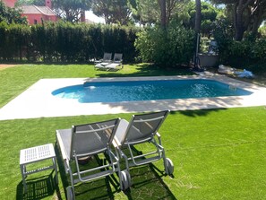 Piscina com duas espreguiçadeiras e uma mesa pequena no quintal.