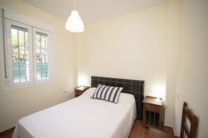 Quarto com cama, mesa de cabeceira, luminária e janela.