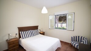 Un dormitorio con cama, mesitas de noche, una silla y un ventanal con cortinas.