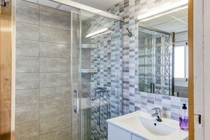 A modern bathroom with a glass-enclosed shower, a white sink, and a tiled backsplash.