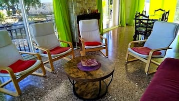 Una habitación con pared de piedra, una mesa redonda con un adorno y dos sillas de madera con cojines rojos.