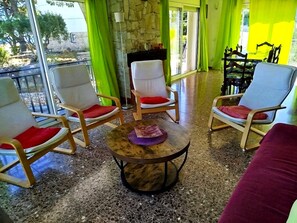 A room with a stone wall, a round table with a decorative item, and two wooden chairs with red cushions.