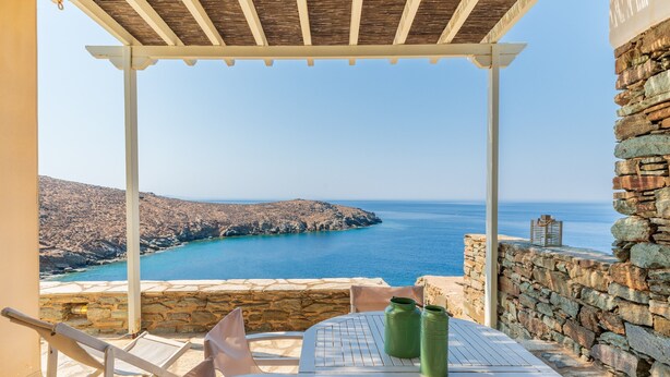 Une terrasse avec une table et des chaises, offrant une vue sur la côte, avec un mur de pierre et un ciel dégagé.