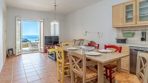 Un coin repas avec une table dressée pour quatre personnes, un téléviseur et une vue sur l’océan.