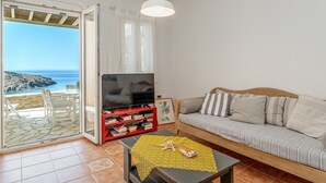 Un salon comprenant un canapé, un téléviseur, une bibliothèque et une vue sur la mer, accessible par une porte coulissante.