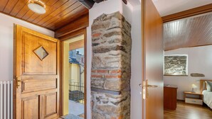 Una porta de fusta, una paret de pedra, un llit, una tauleta de nit i una finestra amb vistes.