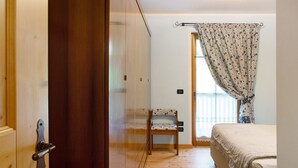 A bedroom with a bed, a chair, a wardrobe, and a window with curtains. - Villa 'Enrica' with Mountain View, Private Terrace and Wi-Fi (Primiero San Martino di Castrozza)