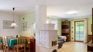 A dining area with a table set for four, a white stove, and a sofa in a room with green walls and a window. - Villa 'Enrica' with Mountain View, Private Terrace and Wi-Fi (Primiero San Martino di Castrozza)