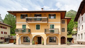 A multi-story building with balconies, arched entrances, and a mountain backdrop. - Villa 'Enrica' with Mountain View, Private Terrace and Wi-Fi (Primiero San Martino di Castrozza)
