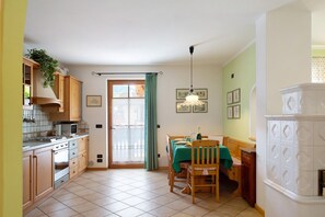 A kitchen with wooden cabinets, a dining table with chairs, a window with curtains, and a hanging light fixture.