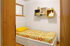 A bedroom with a bed, a window with lace curtains, and two wall-mounted shelves with decorative items.