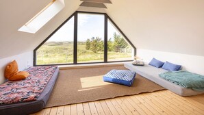Ein Schlafzimmer im Spitzboden mit geneigter Decke, großem Fenster, einer Couch, einem Bett und Holzboden.