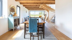 Ein Essbereich mit einem Holztisch, Stühlen, einer blauen Tischdecke, einem Schrank mit Spiegel und einer Treppe, die zu einem Außenbereich führt.