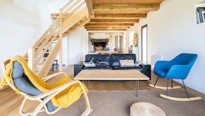 Ein modernes Wohnzimmer mit einer Holztreppe, einem Kamin, einer Couch, einem Schaukelstuhl und einem blauen Sessel.