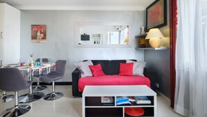 Un salon moderne avec un canapé noir, des coussins rouges, une table basse blanche et un coin repas comprenant une table et des chaises.