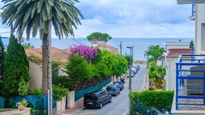 Une rue côtière bordée de voitures garées, avec un palmier et un immeuble doté d’un balcon.