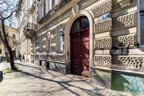 Edificio histórico con puerta roja, fachada de piedra y un letrero azul que indica la dirección.