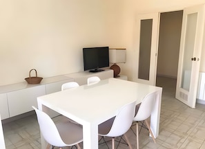 A modern dining area with a white table and chairs, a television on a stand, and a basket on the counter.