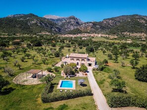 Une grande maison avec une piscine, entourée d’une pelouse bien entretenue et d’arbres, avec des montagnes en toile de fond.