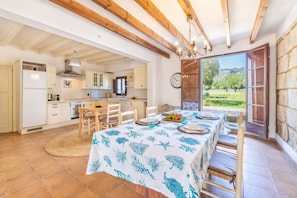 Une cuisine avec des poutres en bois, une table à manger dressée pour quatre personnes et une vue sur un jardin par une porte ouverte.
