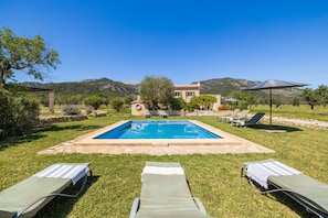 Une piscine entourée de chaises longues, un sentier en pierre et une chaîne de montagnes en arrière-plan.