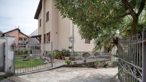 Un patio con suelo de piedra, puertas de metal, plantas en macetas y un edificio con fachada de color claro.