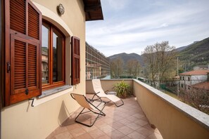 Ein Balkon mit zwei Liegestühlen, einem Blumentopf und Blick auf Berg und Stadt.
