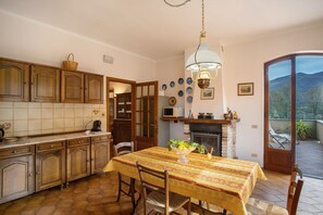 A kitchen with wooden cabinets, a tiled backsplash, a dining table with a yellow tablecloth, and a fireplace.
