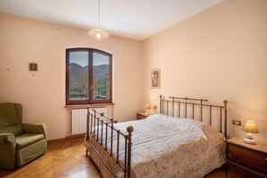 A bedroom with a bed, a chair, a window with a view, and a bedside lamp.