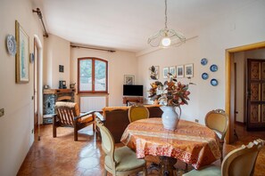 A dining area with a table set for four, surrounded by chairs, a vase with flowers, and a television on a stand.