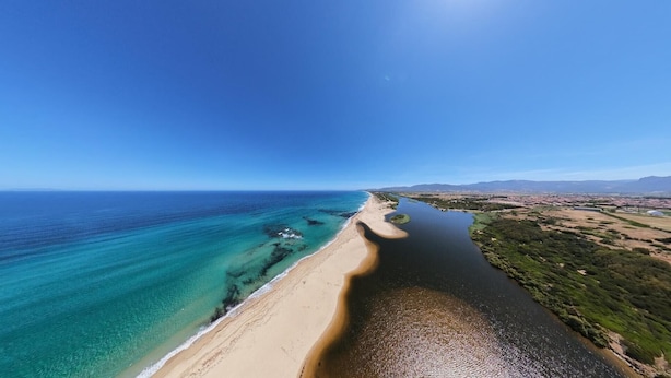 Paisaje costero con playa, aguas azules cristalinas y montañas a lo lejos.